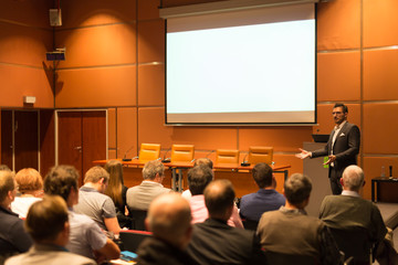Speaker giving a talk in conference hall at business event. Audience at the conference hall. Business and Entrepreneurship concept. Copy space on white screen.