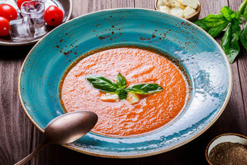 Tomato gazpacho soup with basil, feta cheese, ice and bread on dark wooden background, Spanish cuisine. Ingredients on table. Top view