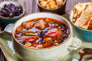 Soup with meat, oregano, chickpeas, peppers and vegetables served with crackers and bread on plate on dark wooden background. Homemade food. Ingredients on table. Top view