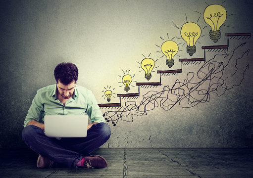 man using laptop growing up light bulbs as symbol of success