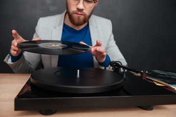 Concentrated young man in glasses using turntable and vinyl record