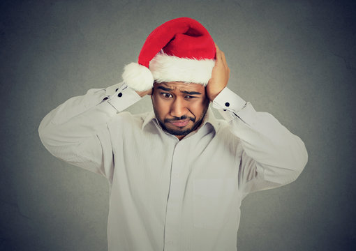 Frustrated man in santa claus hat covering ears to block noise