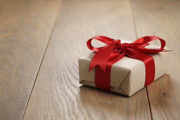 rustic craft paper gift box with red ribbon bow on wood table, shallow focus