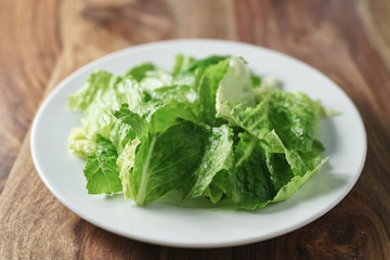 torn romaine lettuce leaves in plate on wood table, diet food