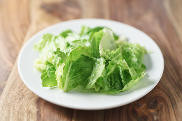 torn romaine lettuce leaves in plate on wood table, diet food