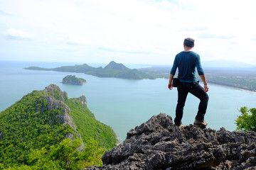 young traveler man standing on the top of mountain at Khao Lom Muak and enjoy the beauty of seascape, travel, freedom, Thailand. The winner, success