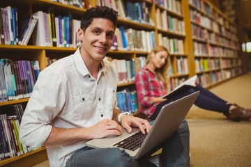 Smiling student using laptop on floor