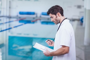 Handsome trainer holding stopwatch and reading clipboard