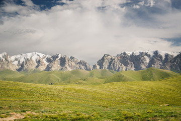 At-Bashi Mountain peaks with snow, green pastures under cloudy sky in Kyrgyzstan