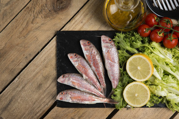 raw red mullet served on curly salad on slate plate on wooden table