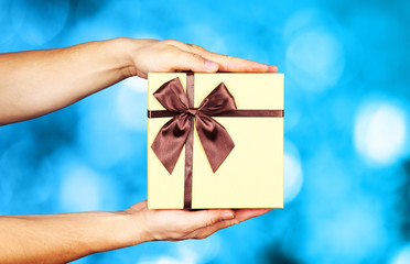 Human hand holding brown ribbon wrapped holiday surprise gift 