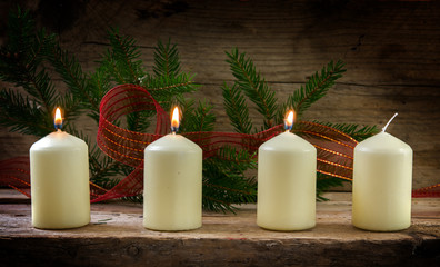 Four white candles, three of them burning on the third advent, christmas decoration on a rustic board 