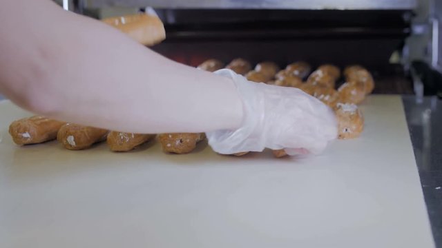 Conveyor line with moving Eclairs. Hands putting eclairs, cakes, pastry, desserts on a production line. 4K.