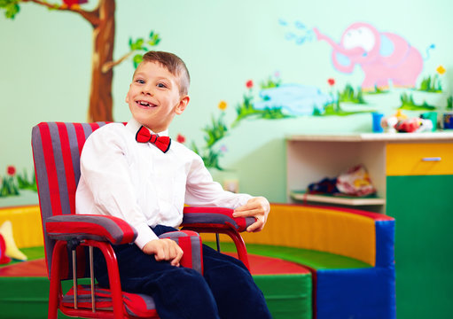 cute happy kid in wheelchair, wearing glad rags in center for children with special needs