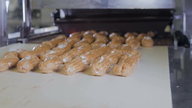 Conveyor line with moving Eclairs. Hands putting eclairs, cakes, pastry, desserts on a production line. 4K.