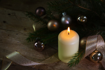 white burning candle for christmas and new year with decoration baubles and ribbon on rustic wood