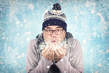 Mann mit Mütze und Schal pustet Schnee aus den Händen