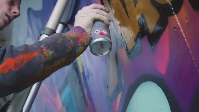 Graffiti artist painting on the wall, exterior, close up