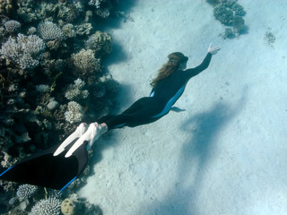 Beautiful girl with monofin swims near coral reef