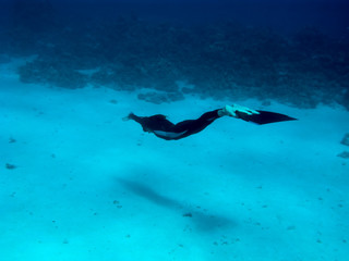 Beautiful freediver girl swims along sea bottom sand