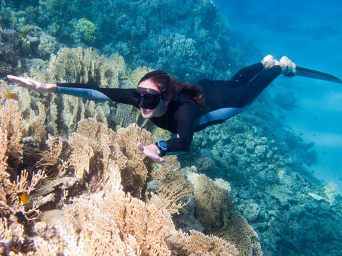 Beautiful girl with monofin swims above corals