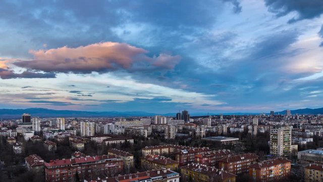 Day to night time-lapse of fast moving clouds in the sky over a city residential area with apartment buildings and streets.