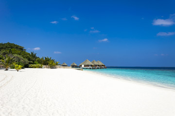 Typically Maldivian Landscape with turquoise ocean, blue sky, white sand beach and beach villas in background.