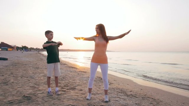 Mother and her sun doing sport exercises on the beach at sunset or sunrise, slow motion