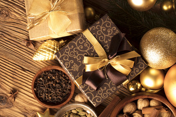 Christmas theme, christmas decoration. presents in boxes on a wooden table with golden baubles, clove, cardamon, star anise, cinnamon. Golden and brownish aesthetics. Place for typography and logo.