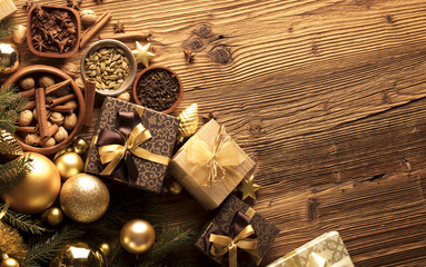 Christmas theme, christmas decoration. presents in boxes on a wooden table with golden baubles, clove, cardamon, star anise, cinnamon. Golden and brownish aesthetics. Place for typography and logo.