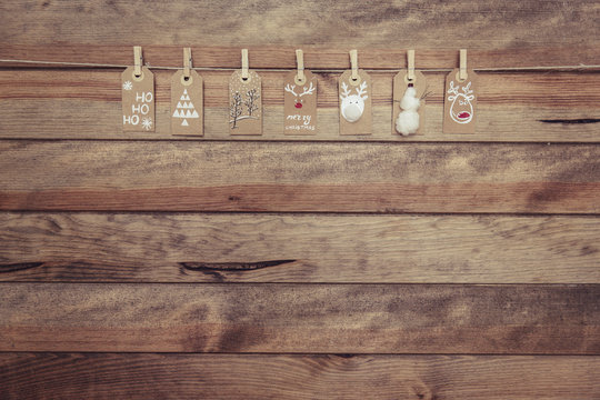 Row of assorted homemade Christmas gift tags hanging on a a wooden wall on a piece of string with clothes pegs 