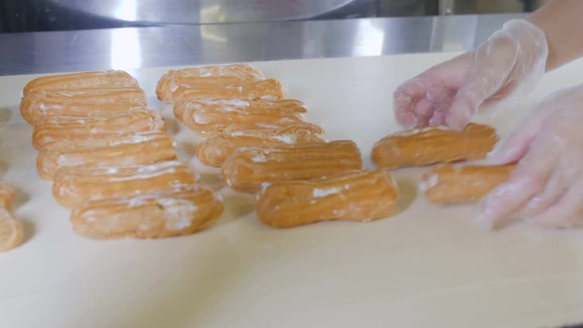 Baker hands putting eclairs, desserts on a production line. Conveyor line with moving Eclairs. 4K.