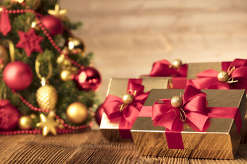 Golden presents with red ribbon under christmas tree. Wooden background and table. Red and gold. Place for typography and logo. Copy space.