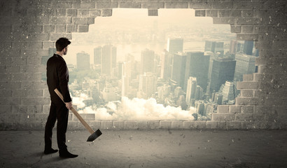 Business man hitting wall with hammer on city view