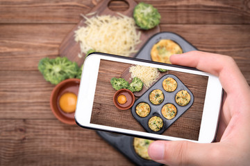 Fototapeta na wymiar Hands taking photo egg muffins broccoli and cheese with smartphone.