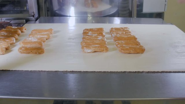 Baker hands putting eclairs, desserts on a production line. Conveyor line with moving Eclairs. 4K.