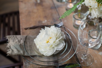 Nice rustic wedding table decorated with beautiful white David Austin roses and candles in glass holders. Rare romantic flowers on plates. Loft style wedding, blurred background.