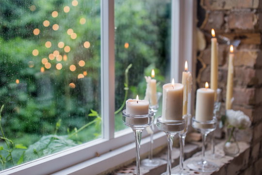 White candles in glass holders. Beautiful rustic wedding decoration. Candle light reflecting in window. Loft style wedding. Blurred background