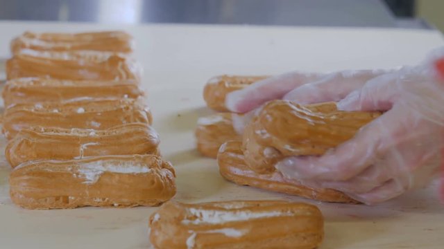 Baker hands putting eclairs, desserts on a production line. Conveyor line with moving Eclairs. 4K.