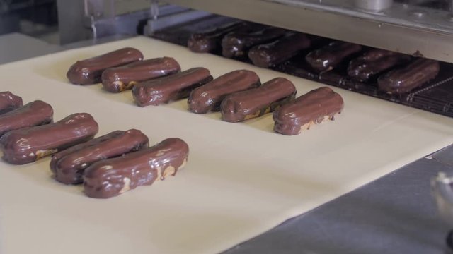Conveyor line with moving Eclairs. Eclairs, cakes, pastry, dessert production line 4K
