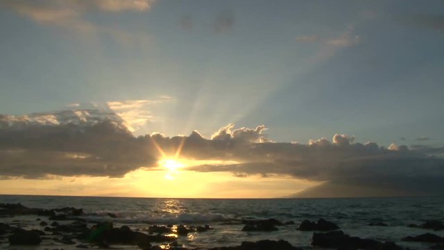 Sun going down over Pacific Ocean from rocky shoreline, time lapse.