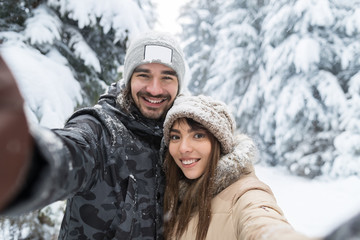 Fototapeta na wymiar Man Taking Selfie Photo Young Romantic Couple Smile Snow Forest Outdoor Winter Pine Woods