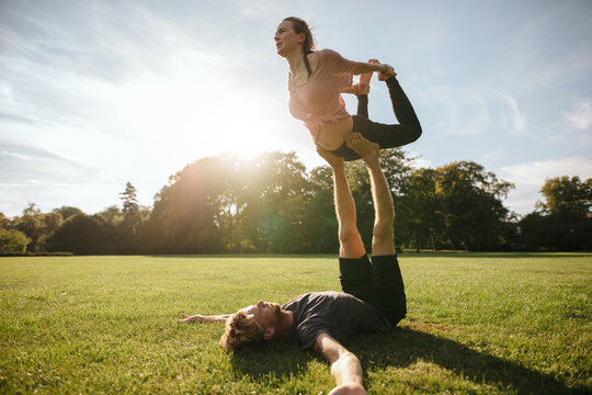 Healthy young couple doing acro yoga on grass
