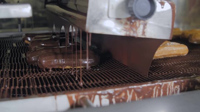 Melted chocolate flowing on fresh creamy eclair cakes on a conveyor at a bakery. 4K.
