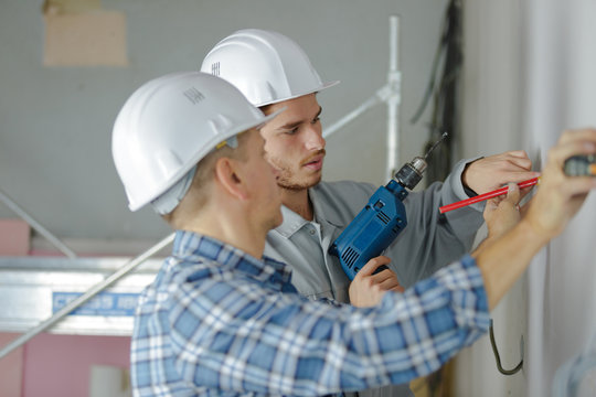 group of builders in hardhats with electric drill indoors