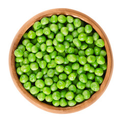 Raw peas in wooden bowl. Green small spherical seeds of the pod fruit Pisum sativum, an edible legume. Isolated macro food photo close up from above on white background.
