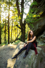 Young tourist with backpack relaxing on rock and enjoying sunset