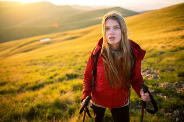 Fototapeta na wymiar Shot of a young woman looking at the landscape while hiking in the mountains. Young tourist with backpack relaxing and enjoying sunset.