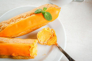 Eclairs with mango cream and  topping on a white wooden table. Drink tea or snack