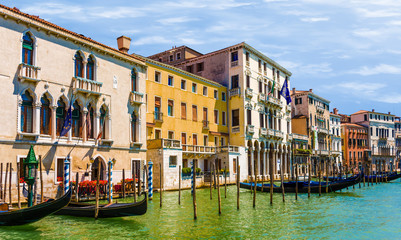 Venice canal with green water and blue sky, colorful houses yellow orange with poles and gondolas and flowers